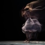 A single female dancer in a white dress with a black background