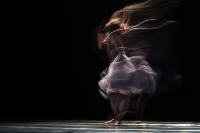 A single female dancer in a white dress with a black background