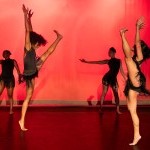 Two women identifying dancers downstage facing each other while lifting their left leg side.  