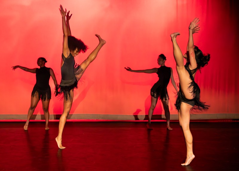 Two women identifying dancers downstage facing each other while lifting their left leg side.  