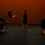 Two artists swaying downstage, two artists rolling up, and one artist is is jumping in the air