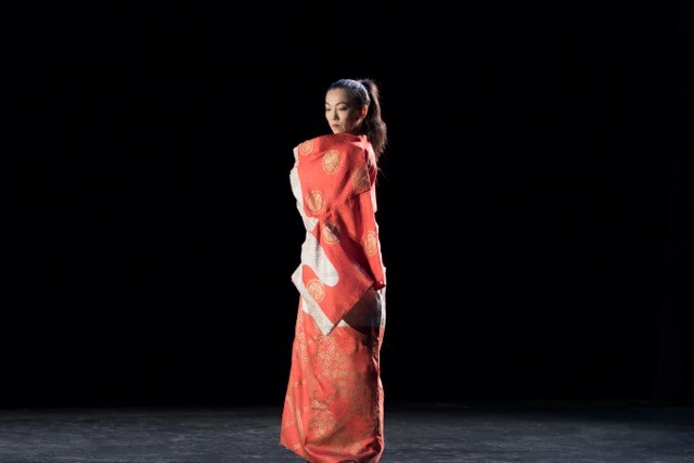 Miki Orihara stand still and center stage as she is wrapped in a long, red, adorned costumed