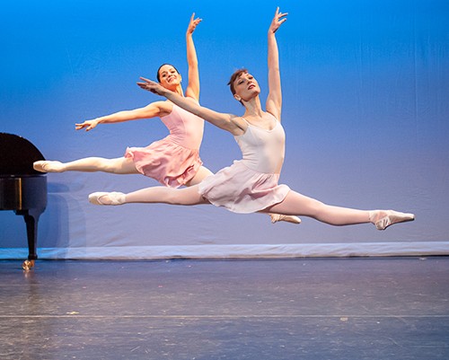 Two female dancers leap across the stage in pastel dresses