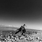 Solo dancer stands on a rocky beach.
