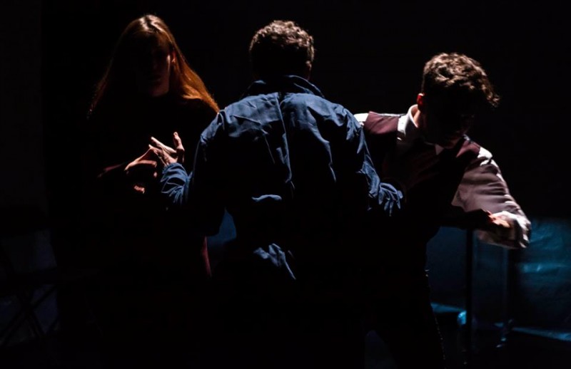 Three Performers struggling against each other in silhouette.