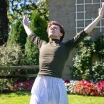 Male dancer standing with arms raised in front of floral backdrop