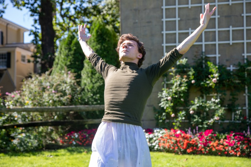 Male dancer standing with arms raised in front of floral backdrop