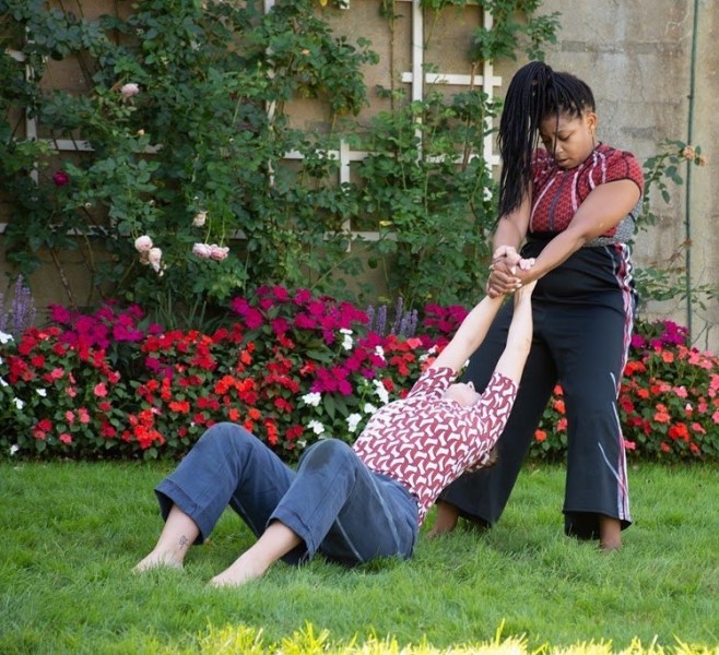 Two dancers connected at the hands, dancing in the grass, in front of flowers