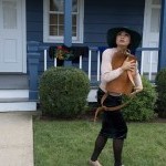 Dancer in hat holding brown leather backpack in front of blue building 