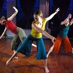 Three dancers in colorful costumes reaching out. 