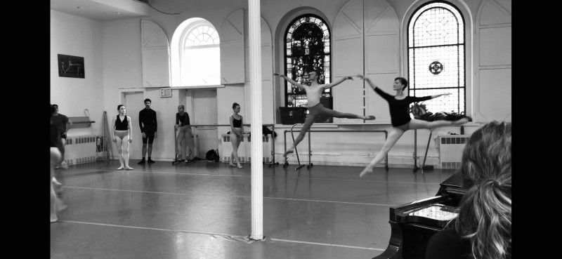 Dancer in arabesque with both arms reaching up and forward on a diagonal. The instructor, Diana Byer, is giving an adjustment