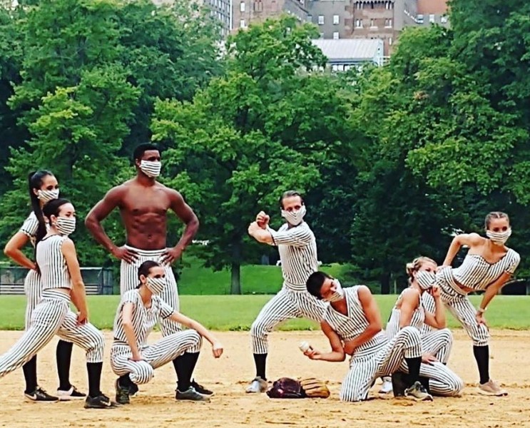 Eight dancers on baseball field in Central Park make different athletic gestures in a group as they take photo together as team.