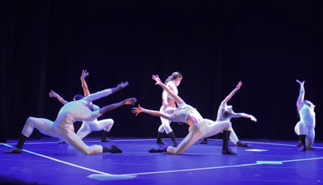 6 dancers, in white pinstriped costumes reach for one another in a low lunge backbend. A baseball diamond is marked onstage.