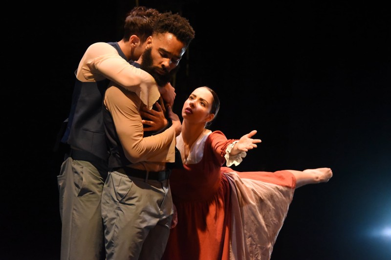 Dancers in an emotional gesture. Two male identifying dancers hold each other as a woman reaches to them. They look away.
