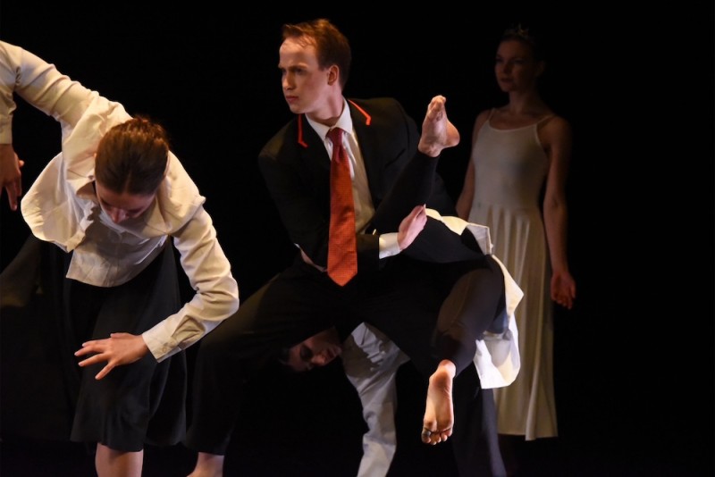 A male identifying dancer in a suit lifting another dancer. 