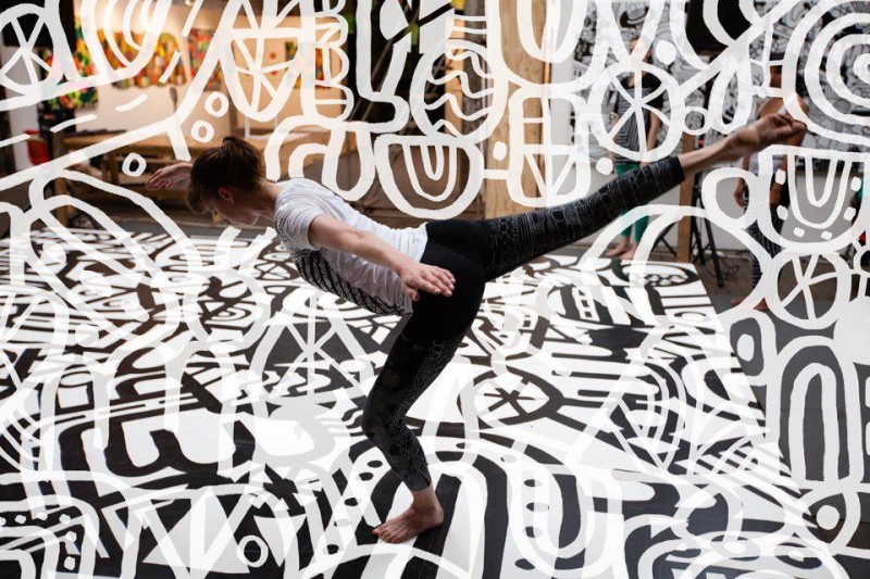 A dancer is in a flat-back arabesque with white designs all around them