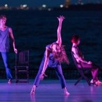 A dancer leans back and reaches upward on center stage.