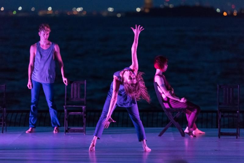 A dancer leans back and reaches upward on center stage.