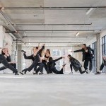 Multiple dancers wearing black attire improvise in a raw space