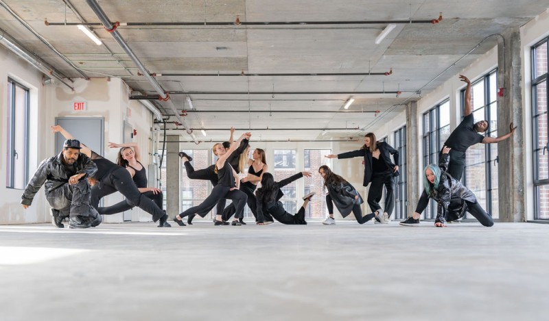 Multiple dancers wearing black attire improvise in a raw space