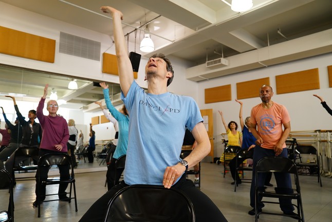 Instructor leading the class to raise their right arm. 