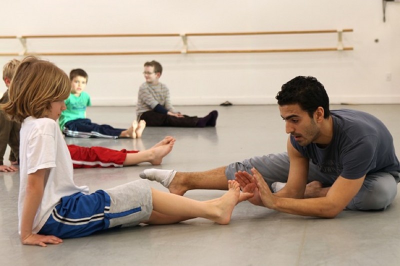 A Teaching Artist works with a young student on pointing his feet.
