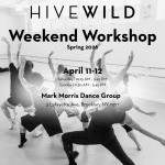 Black and white image, 8 dancers in a clump lunging with their arms up and backs facing the camera