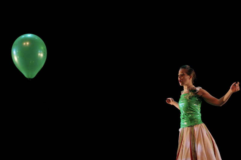 A person in a green dress sees a green balloon floating away
