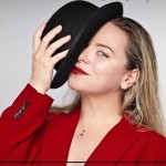 Close up image of Artistic Director Zanza Steinberg in a red blazer with a black bowler hat over one eye