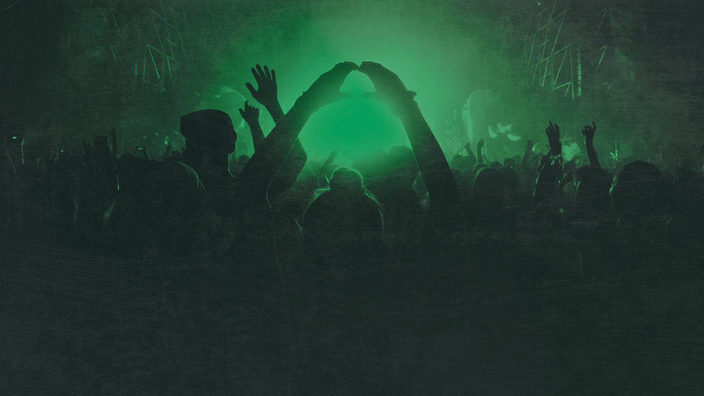 Photo taken from behind a crowd at a concert. A green light emits from the stage in front of them.