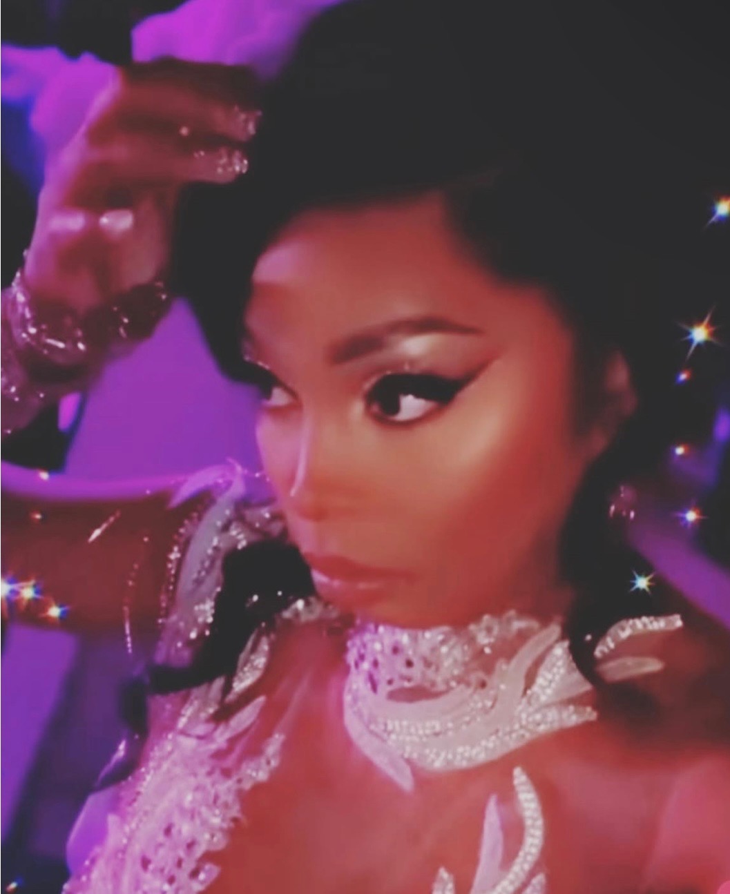 Courtney looks to the side with one hand touching the top of her head. She has black hair in an upswept ponytail and her shoulders are adorned in sequined appliques.